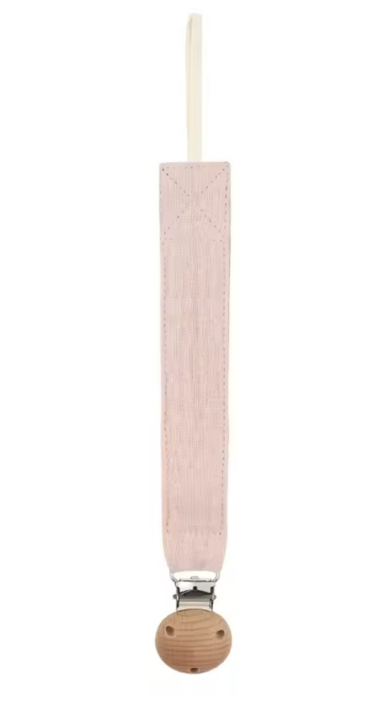 Attache-sucette en tissu rose pâle, longue et étroite, avec une boucle en haut et un clip métallique fixé sur une pièce ronde en bois.