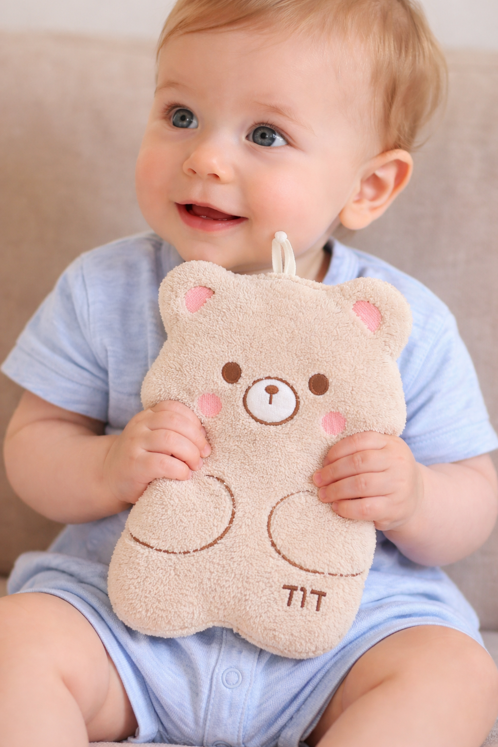 Bébé souriant tenant un doudou ours beige personnalisé avec broderie, doux et adapté dès la naissance, idéal comme cadeau bébé