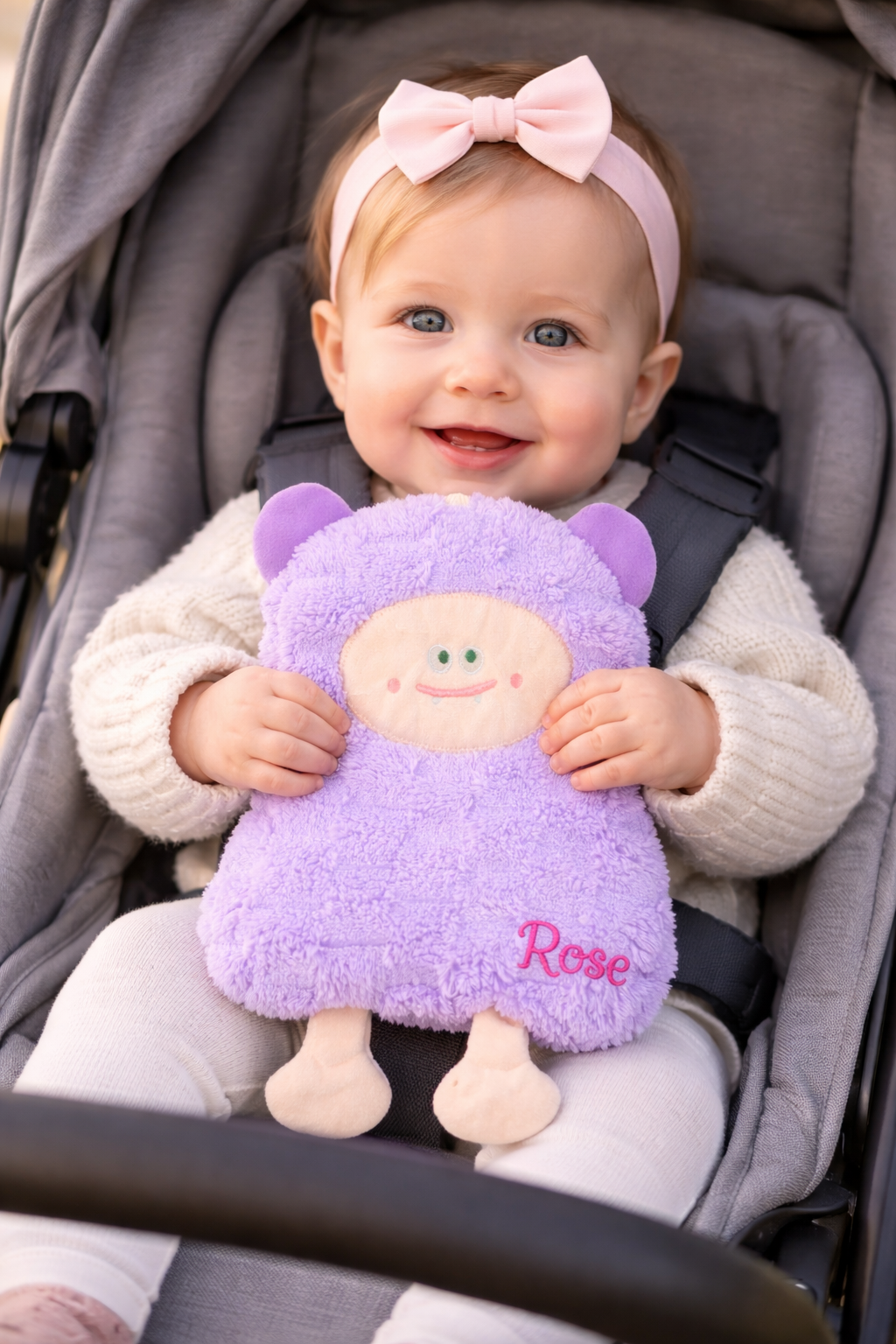 Bébé d’un an assis dans une poussette tenant une peluche violette avec le prénom Rose brodé