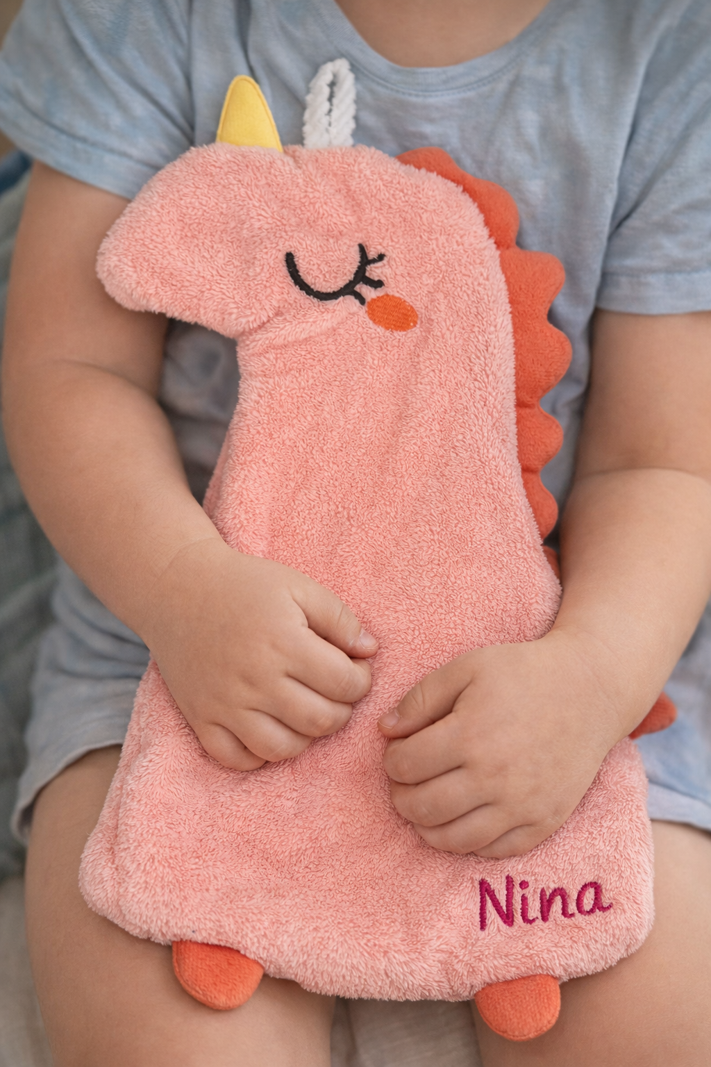 Enfant tenant un doudou dinosaure rose doux avec le prénom Nina brodé en rose foncé en bas à droite