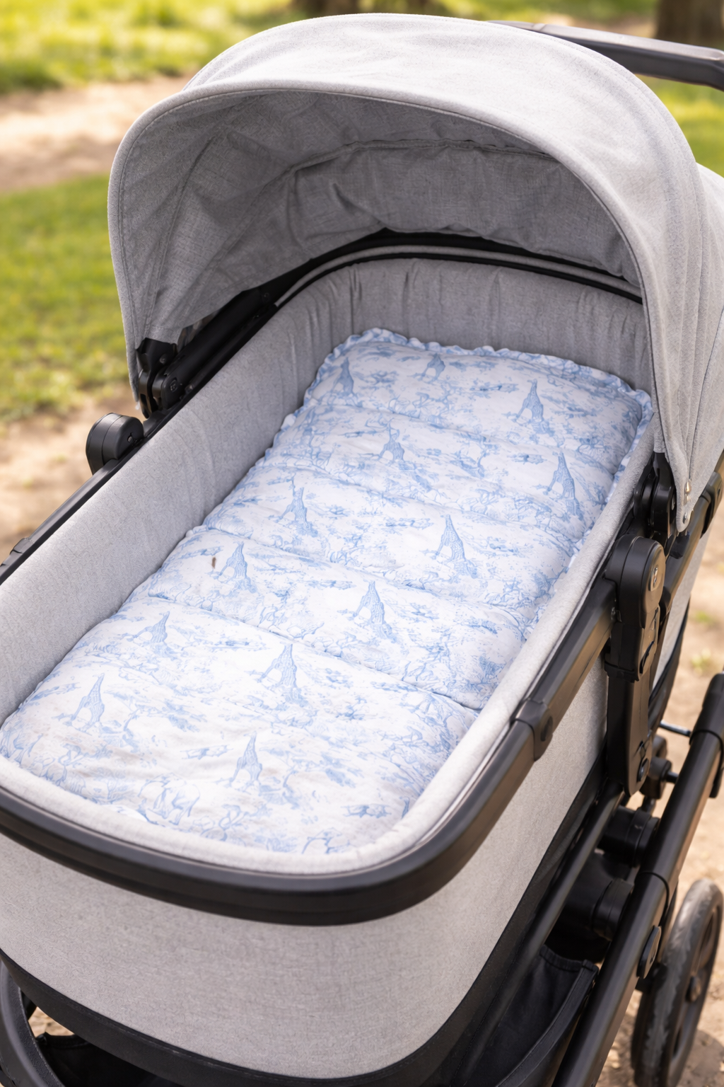 Matelas rembourré pour nacelle de poussette, blanc avec imprimé safari bleu, installé dans une nacelle grise en extérieur.