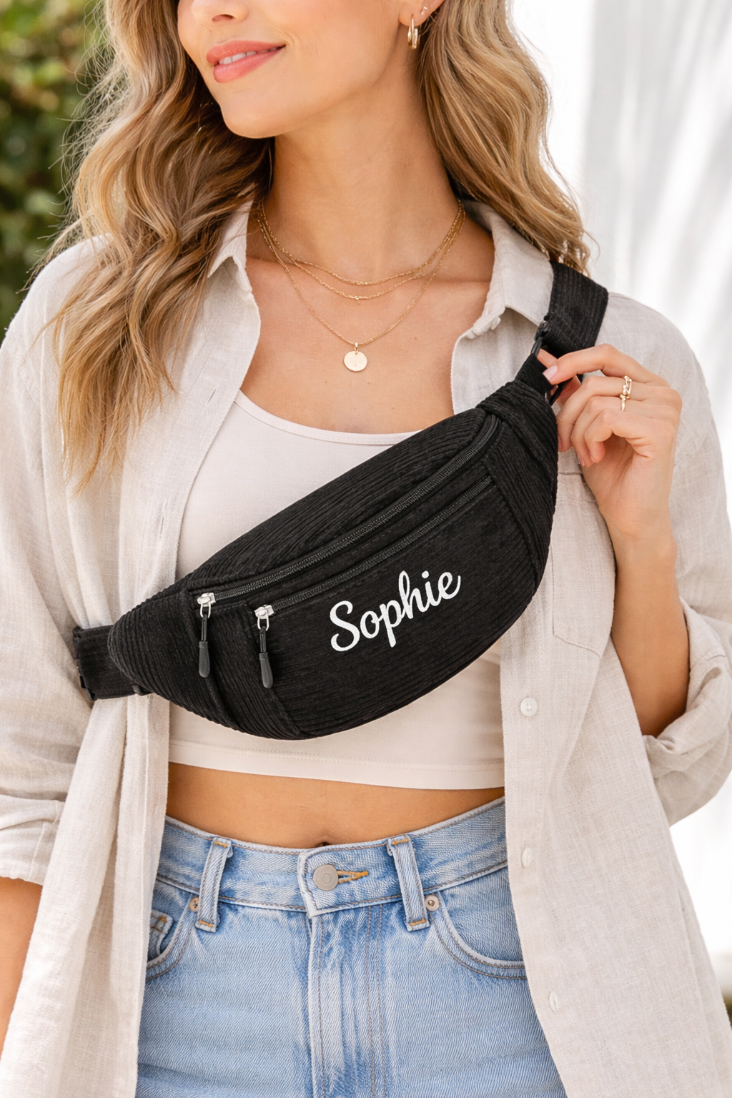 Femme portant un sac banane noir en velours côtelé avec le prénom Sophie brodé en blanc sur la poche avant