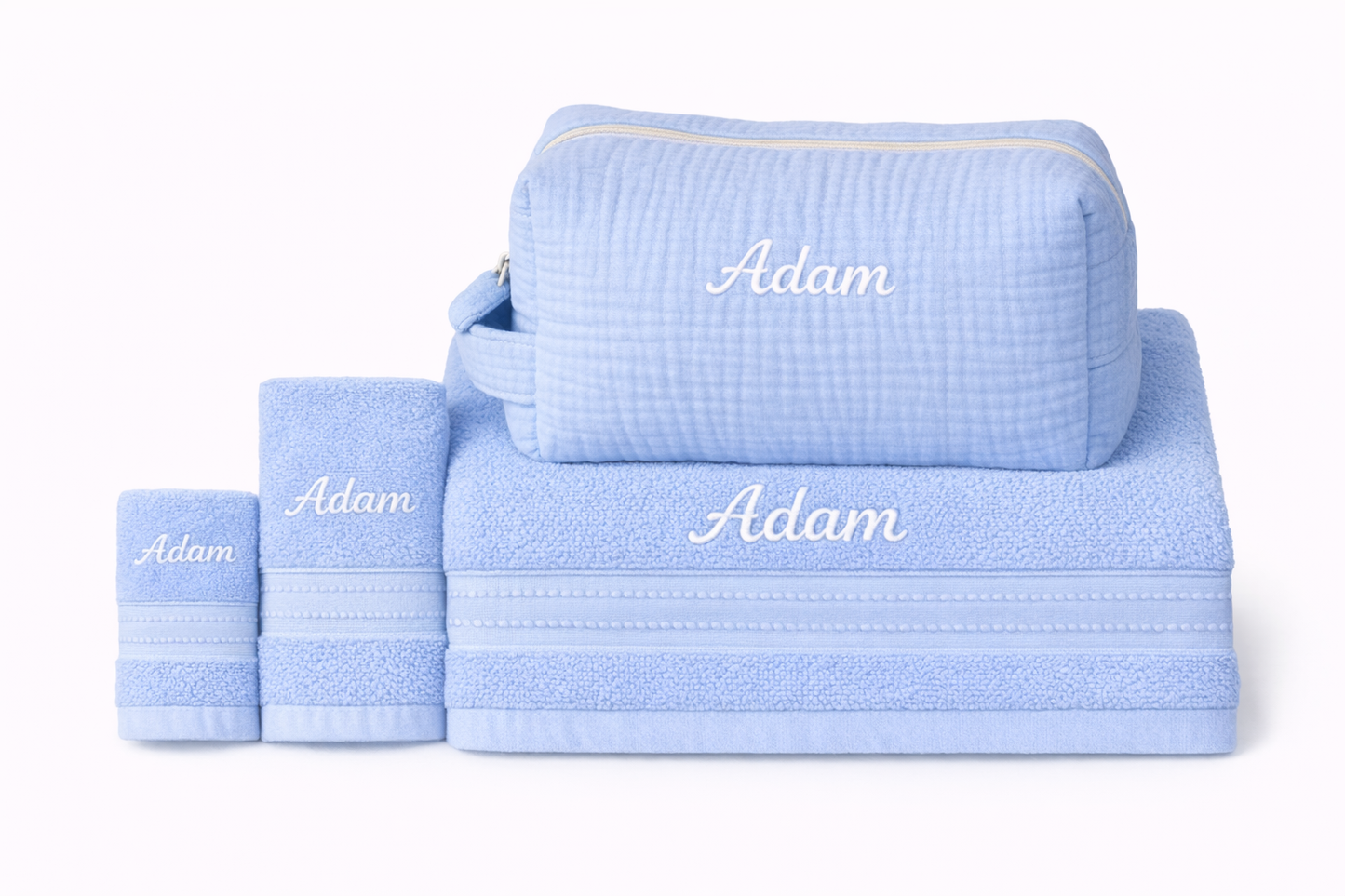 Ensemble de serviettes bleues personnalisées avec le prénom "Adam" brodé, accompagné d’une trousse de toilette assortie posée sur la grande serviette.