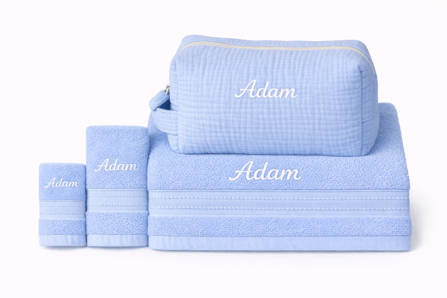 Ensemble de serviettes bleues personnalisées avec le prénom "Adam" brodé, accompagné d’une trousse de toilette assortie posée sur la grande serviette.