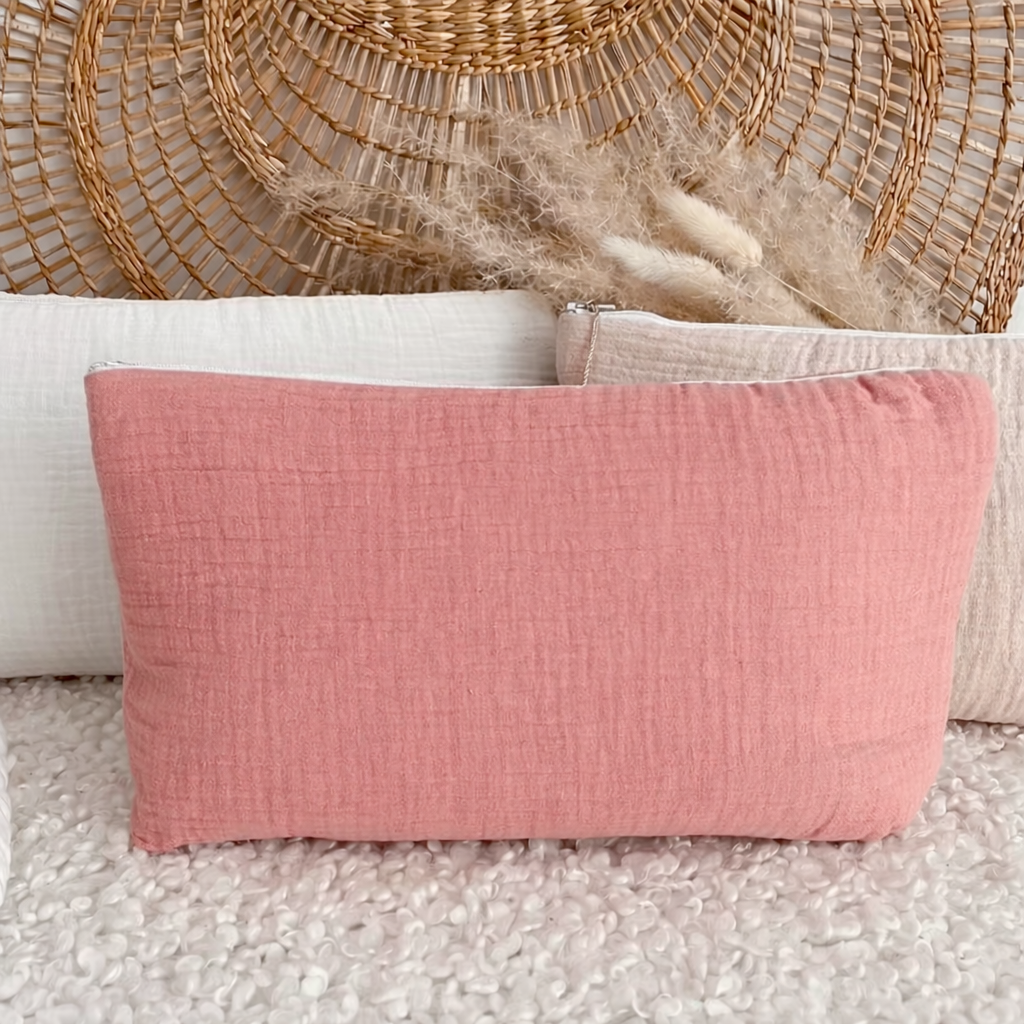 Trousse rose poudré en gaze de coton avec texture gaufrée, posée sur tissu blanc avec décoration naturelle en arrière-plan