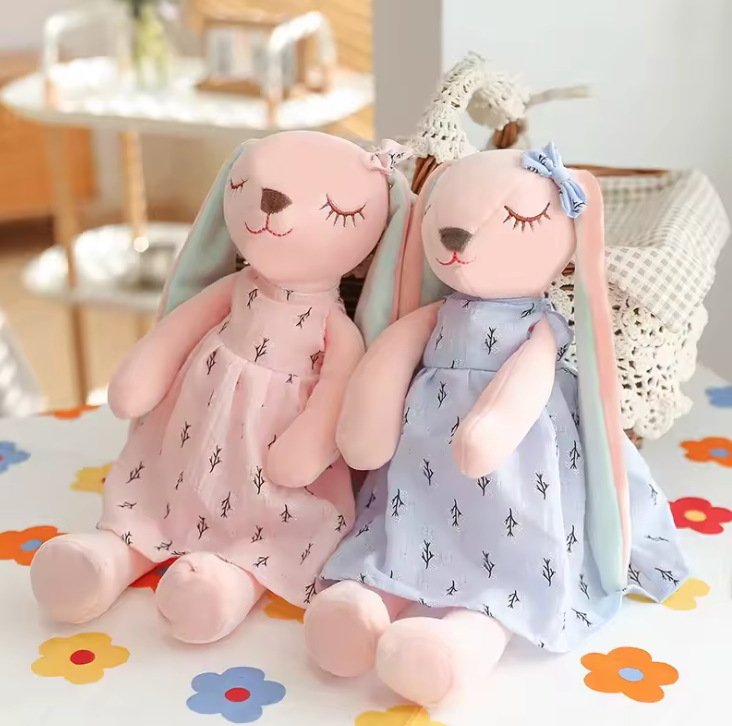 lot Peluche en forme de lapin rose portant une robe, avec de longues oreilles et un nœud sur la tête, assise sur fond blanc.